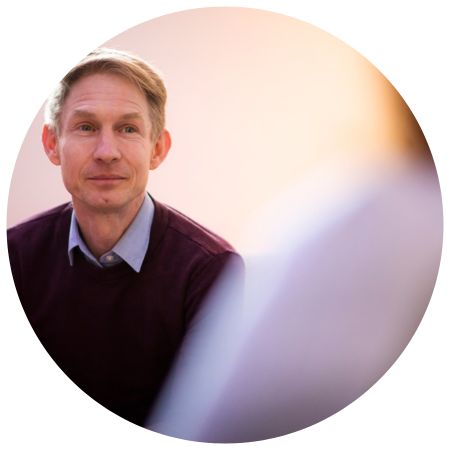 Hoofd en schouders van een glimlachende Ron Meijering in een bordeauxrode trui, zittend in een gesprek.