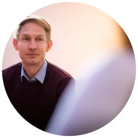 Hoofd en schouders van een glimlachende Ron Meijering in een bordeauxrode trui, zittend in een gesprek.